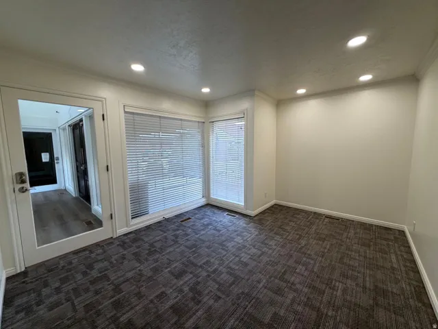 Recessed lighting, patterned carpet flooring, large windows with blinds, a glass-paneled door, and a light-toned wall finish