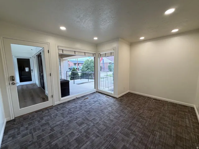 Recessed lighting, crown molding, gray patterned carpet, glass panel door, and large sliding glass door
