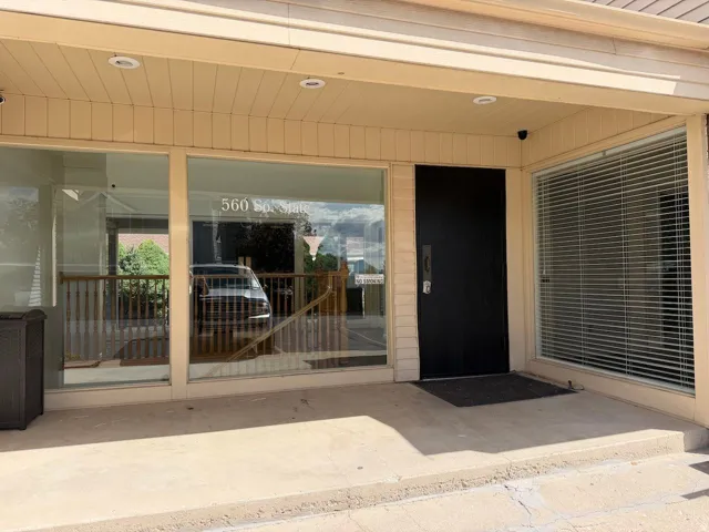 Recessed lighting, a solid entry door, a large storefront window, horizontal window blinds, and an exterior security camera