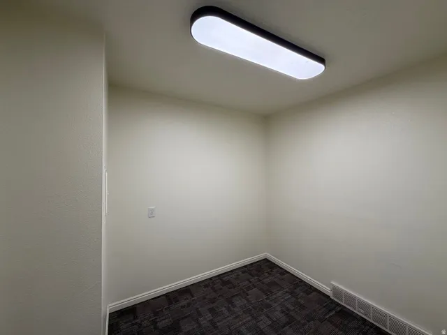 Recessed ceiling light fixture, textured off-white walls, dark patterned carpet, and white trim