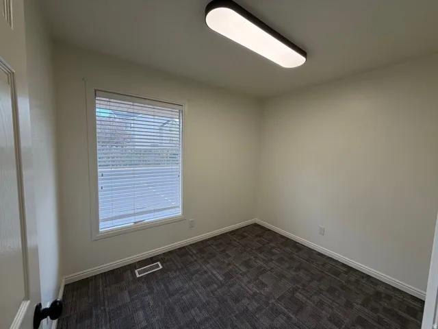Neutral painted walls with a rectangular window, equipped with horizontal blinds, and a contemporary ceiling-mounted light fixture