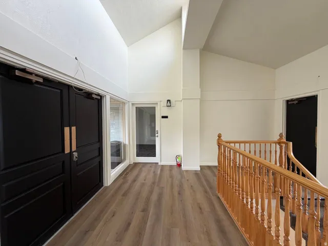 Vaulted ceiling, wood-finish flooring, natural wood staircase, dark-paneled double doors, and white walls