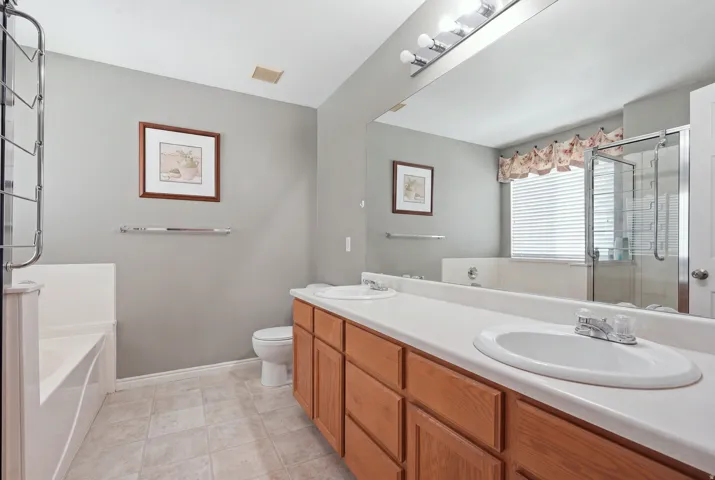 Dual undermount sinks with chrome fixtures, wood-finish cabinetry, extensive vanity mirror, tile flooring, and a separate shower enclosure