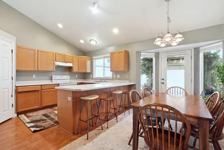 Vaulted ceiling with recessed lighting, wood-finish cabinetry, white countertops, kitchen island with seating, and a bay window with an exterior door