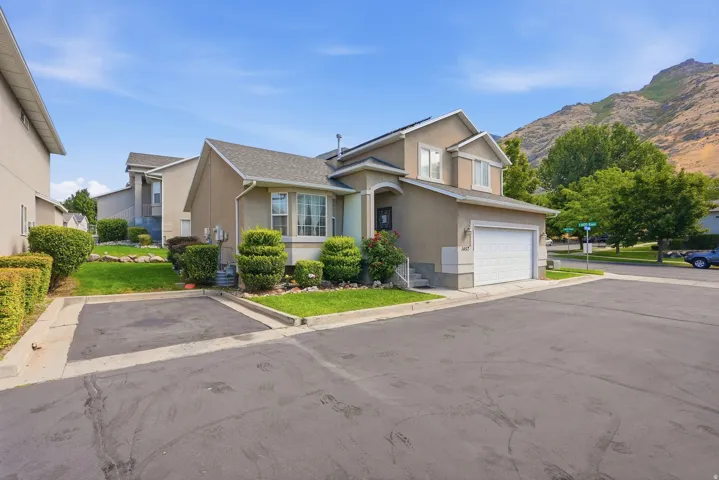 Exterior featuring a two-story stucco facade, an attached garage, landscaped shrubbery, a bay window, and a prominent mountain backdrop