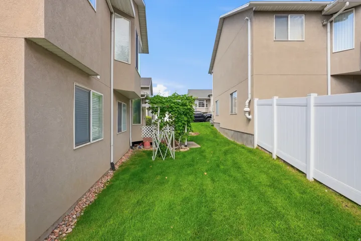 Expansive grass area featuring a white privacy fence and stucco exterior