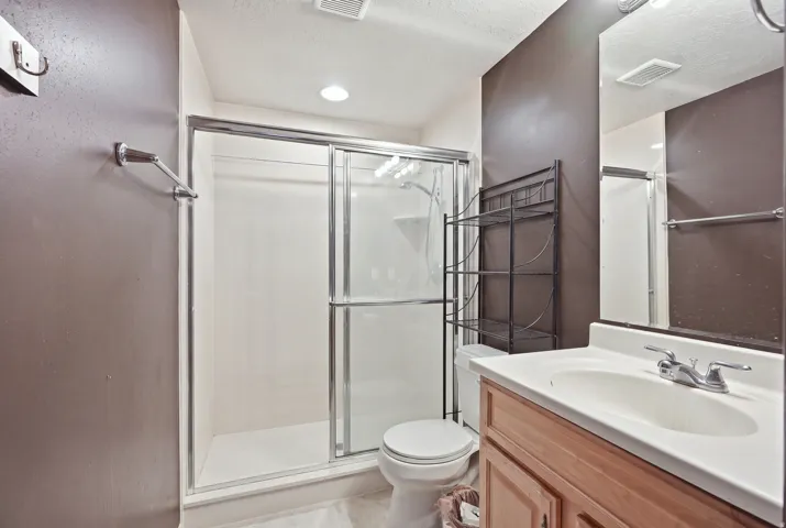 Full shower enclosure with sliding glass doors, single vanity with integrated sink, wood-finish cabinetry, and wall-mounted mirror