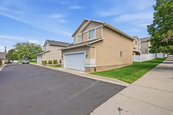 Two-story stucco exterior with an attached garage, featuring a white garage door, and a sidewalk border