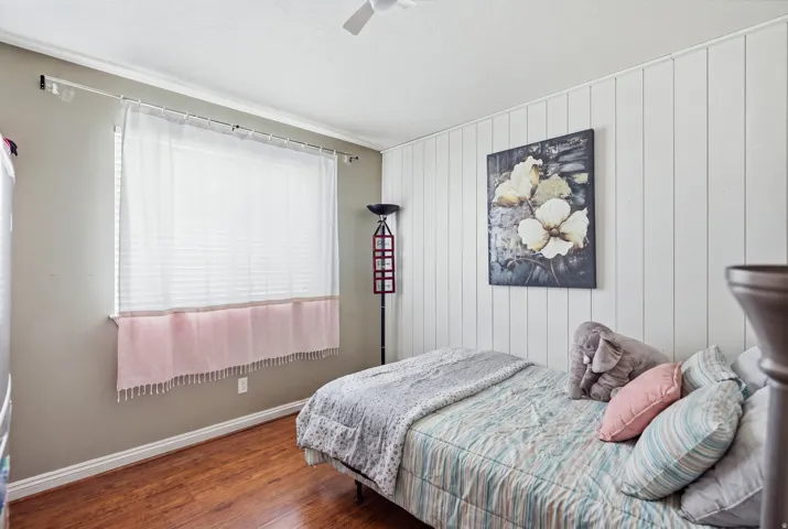 Wood-finish flooring, white crown molding, a window with horizontal blinds, and a white paneled accent wall