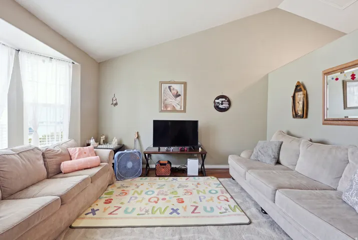 Vaulted ceiling with neutral paint colors, bay window with window treatments, and light wood-finish flooring