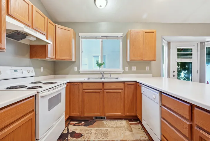 Full kitchen with wood cabinetry, white countertops, built-in dishwasher, and a window above the sink