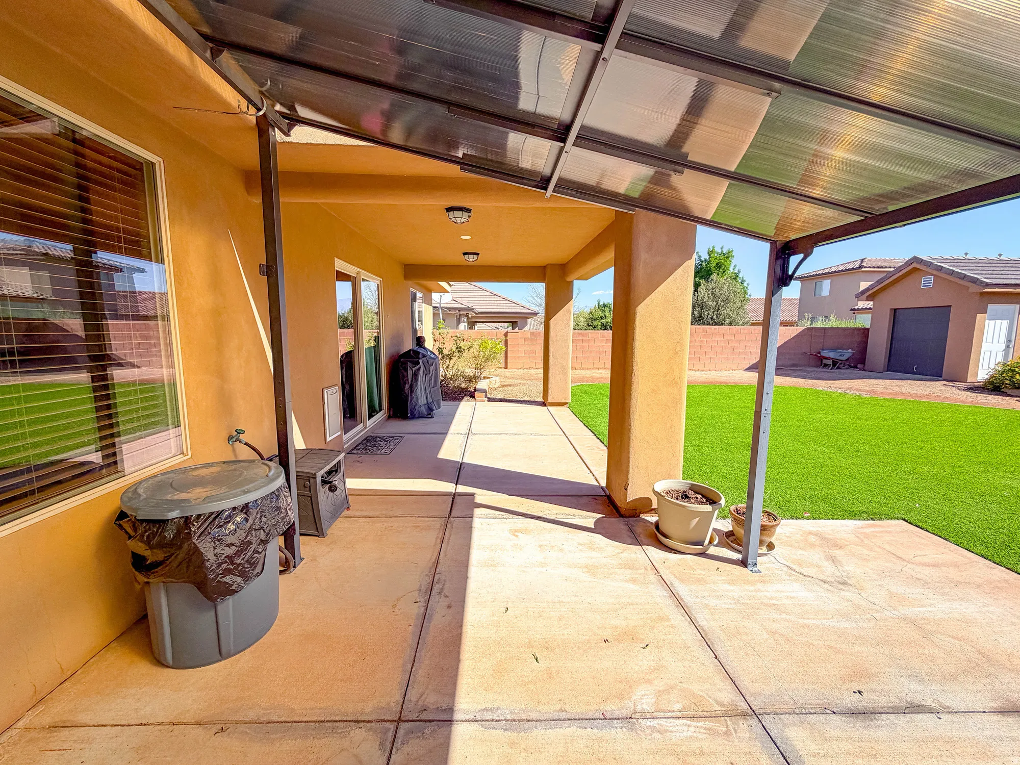 Expansive covered patio with recessed lighting, concrete flooring, and a large artificial turf area