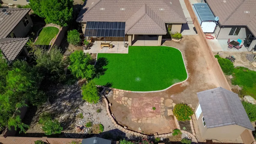 Rear exterior featuring a covered patio, artificial turf lawn, stone paver patio, and detached storage shed
