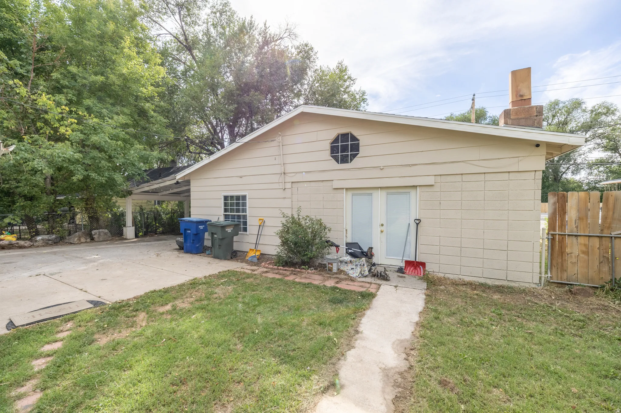 Rear exterior with a concrete patio, double French doors, an octagonal window, and a covered carport