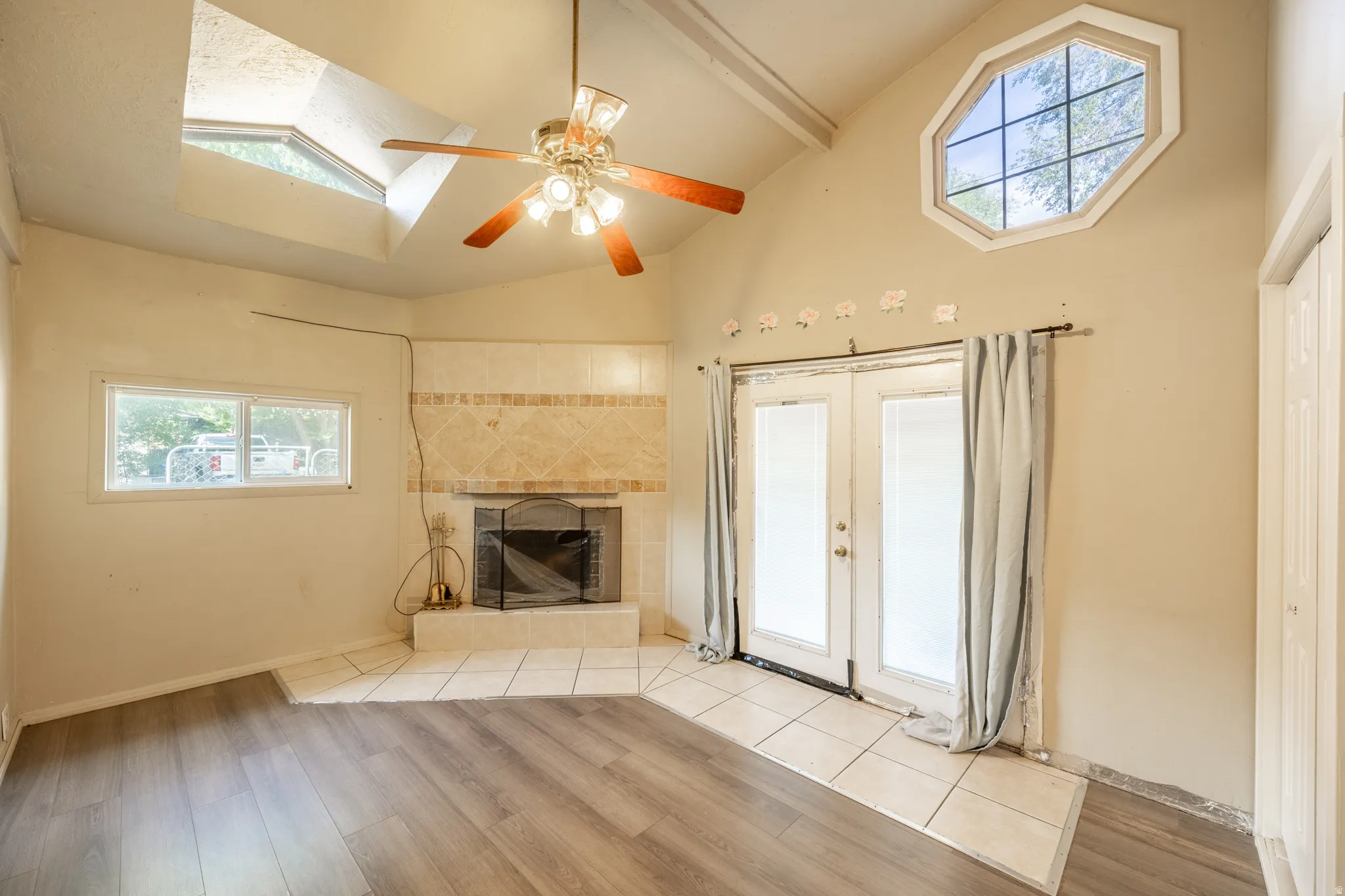 Vaulted ceilings, wood-finish flooring, a corner fireplace with tile surround, French doors, and an octagonal upper window