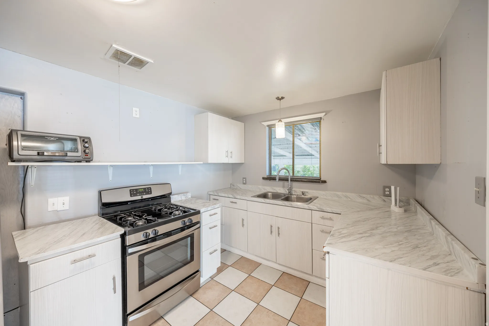 Kitchen featuring a stainless steel range, dual basin sink, patterned tile flooring, white cabinetry, and light-toned countertops