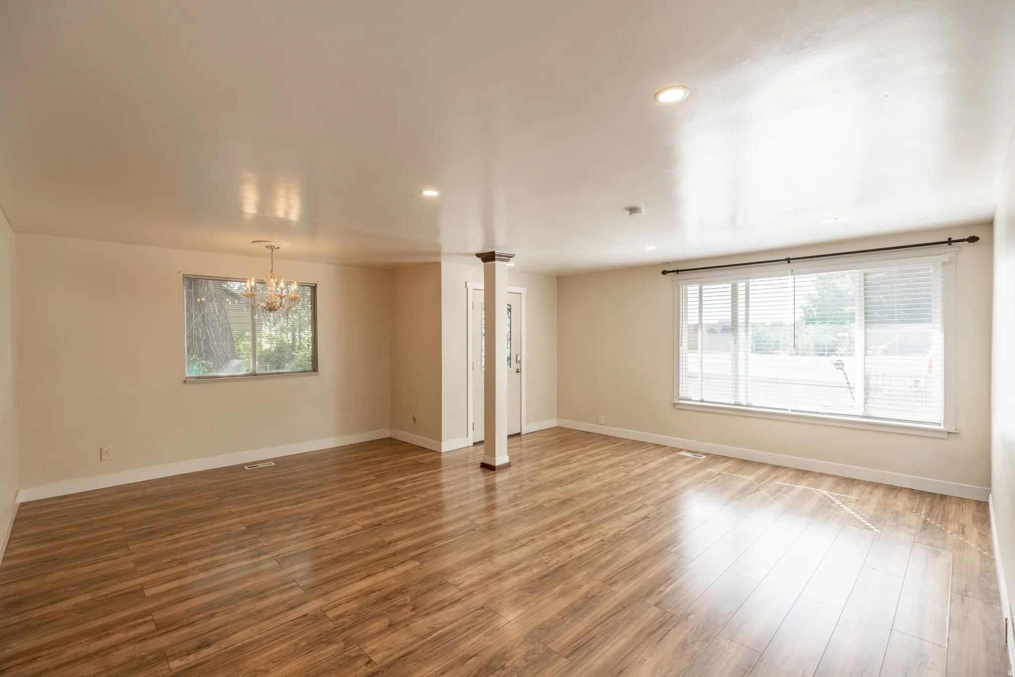 Wood-finish flooring, recessed lighting, chandelier, and multiple windows with blinds
