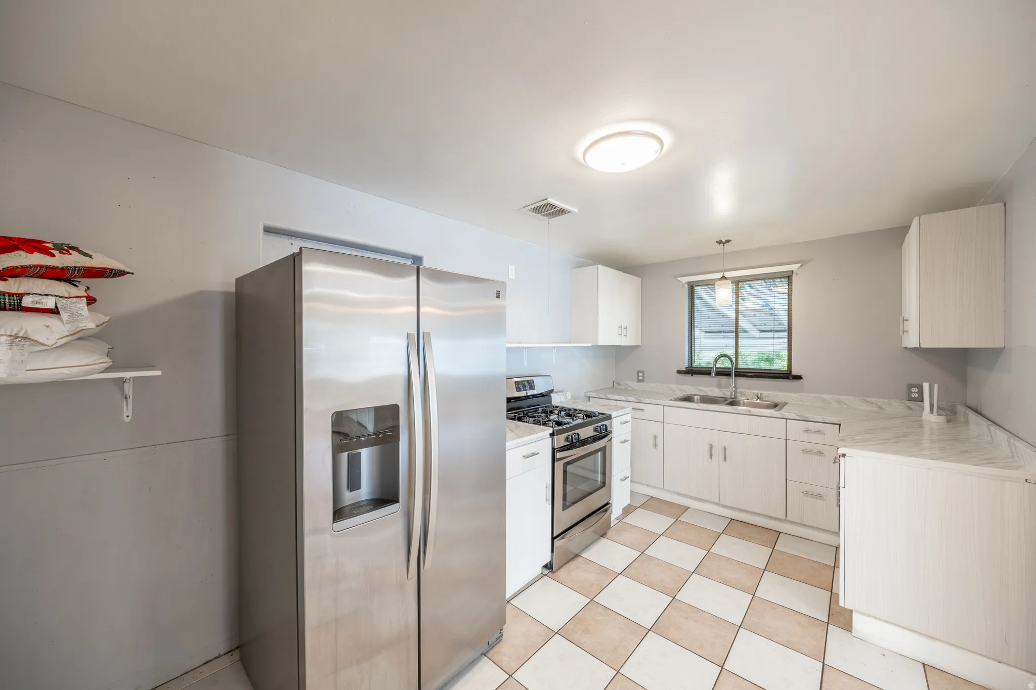 Stainless steel refrigerator, stainless steel range, white cabinetry, tile flooring, and a single basin sink