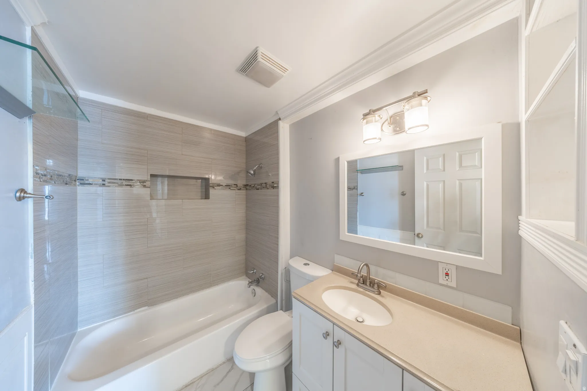Full bathroom featuring a white vanity with an integrated sink, a framed mirror, and a full bathtub with tile surround and a tiled niche