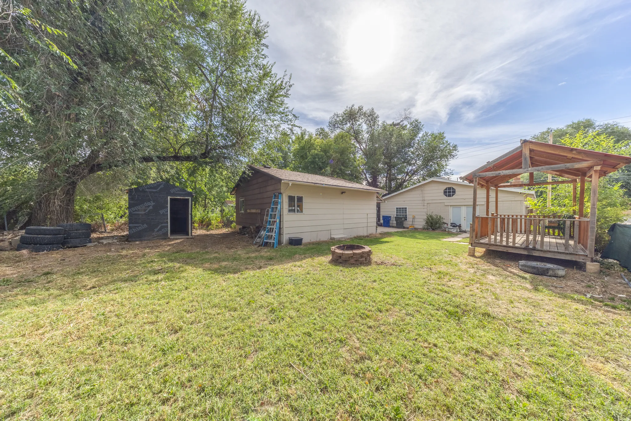 Spacious yard with a wooden gazebo, dedicated fire pit, mature trees, and two storage sheds