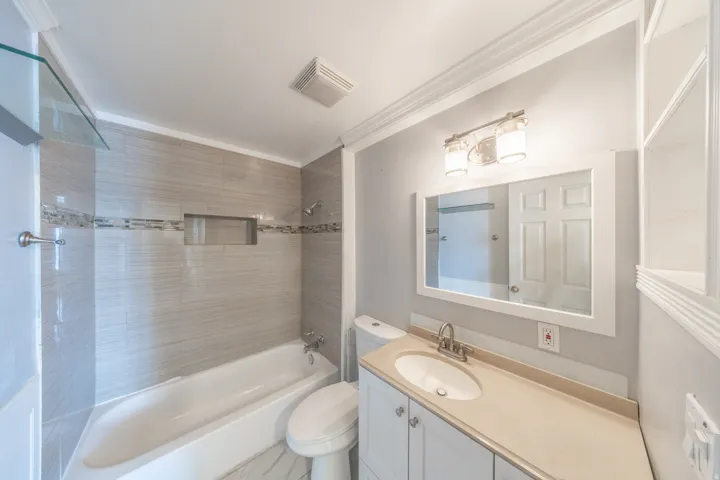 Full bathroom featuring a white vanity with an integrated sink, a framed mirror, and a full bathtub with tile surround and a tiled niche