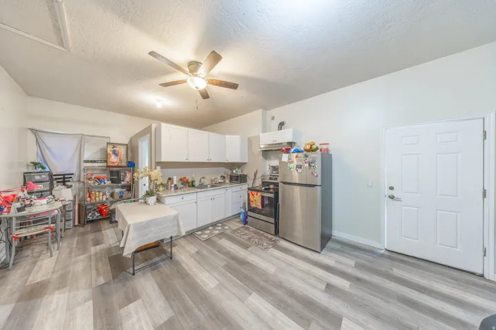 Wood-finish flooring, white cabinetry, stainless steel appliances, ceiling fan, and white paneled door