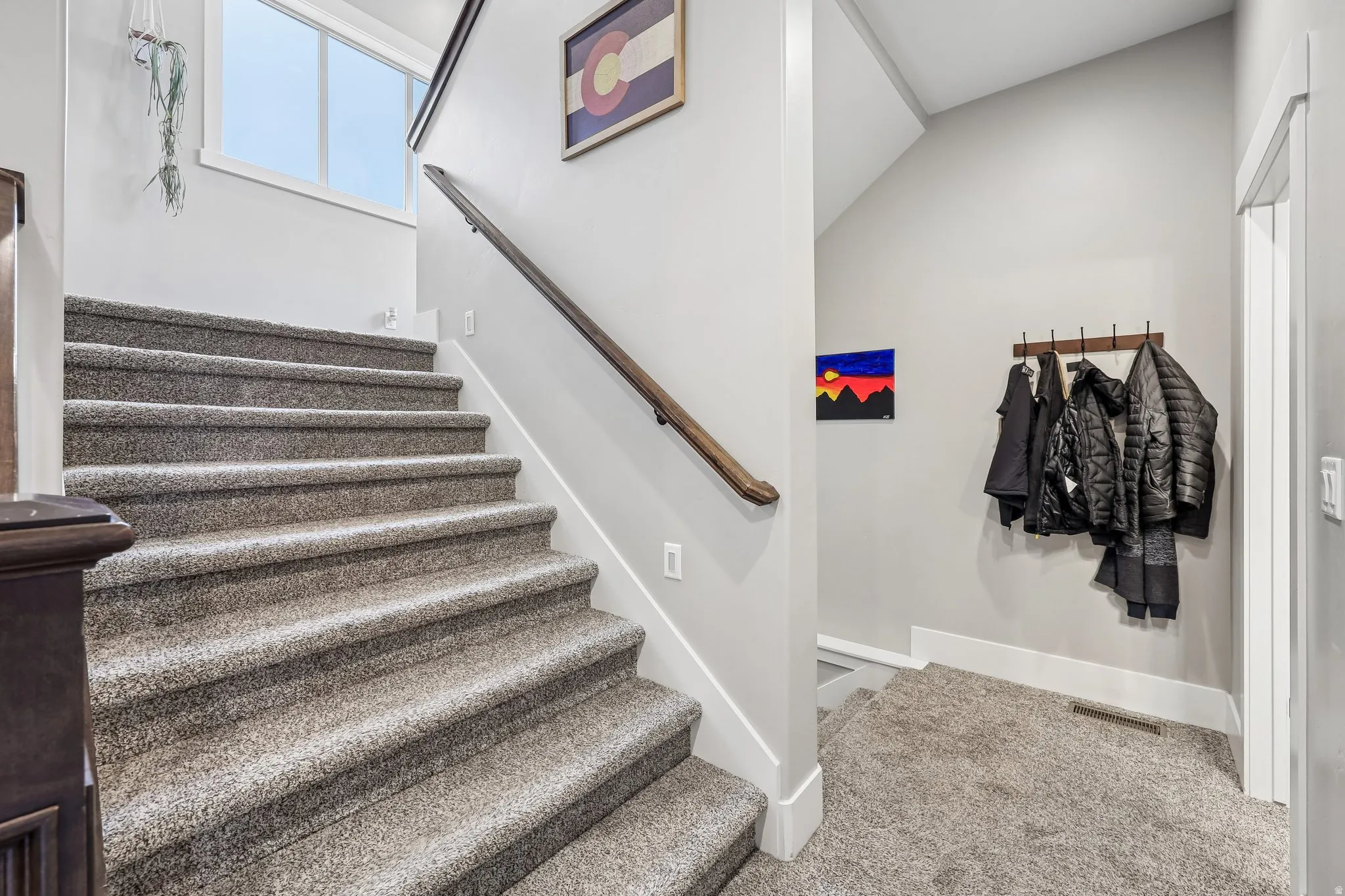 Carpeted staircase with a wood handrail and transom window connecting three levels inside a Rustler at Hideout home in Hideout, Utah.
