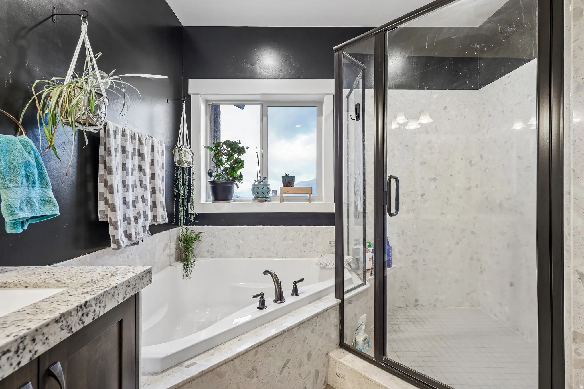 Primary bathroom with a recessed soaking tub, matte black fixtures, a separate glass-enclosed shower and a window above the tub, in Hideout, Utah.