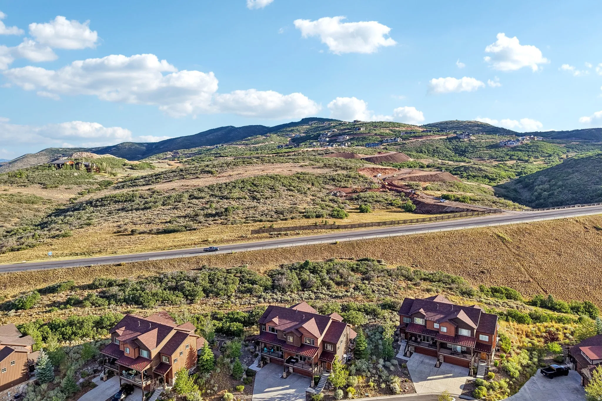 Wide aerial of terraced homes with multi-level decks in Rustler at Hideout, set against open hillside and a mountain backdrop.