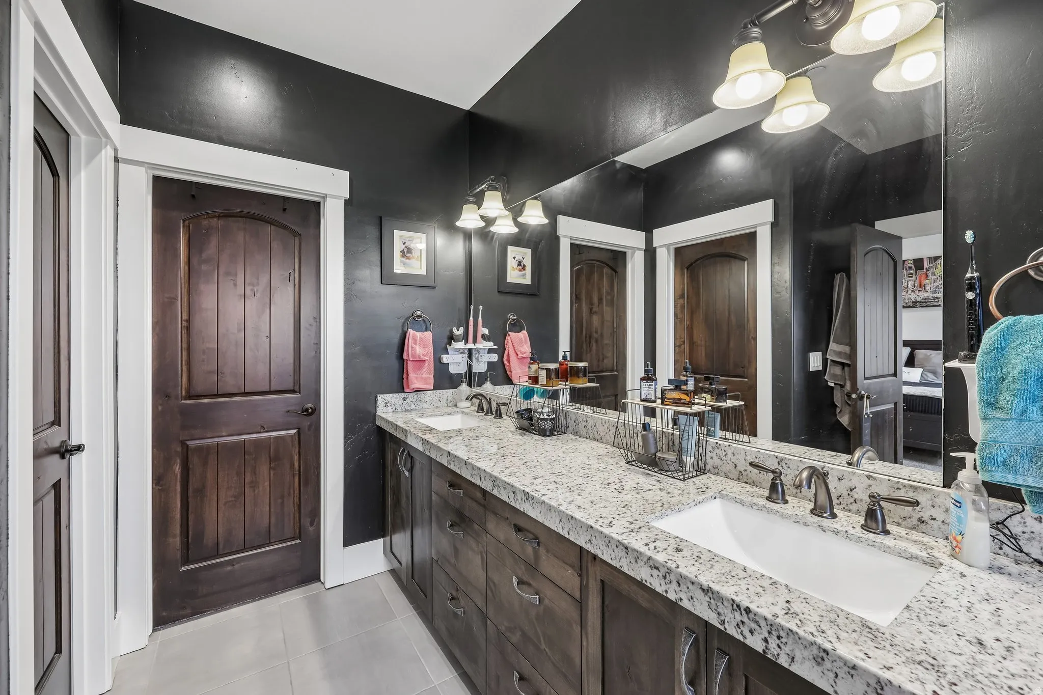 Primary bathroom with a double vanity, speckled stone countertop, dark wood cabinetry and a large mirror in a Rustler at Hideout home.