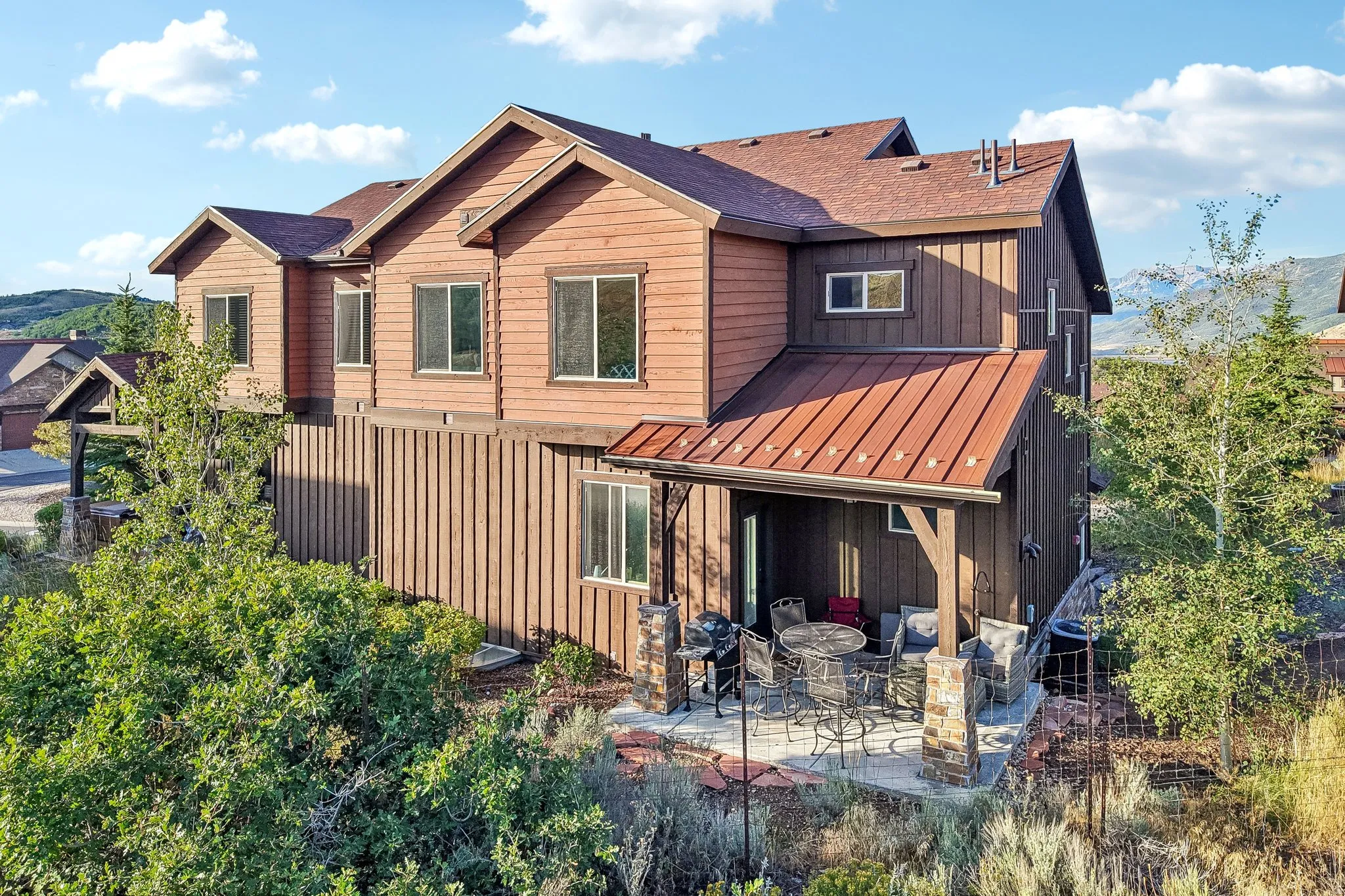 Multi-level exterior with wood siding, a covered patio with stone-clad pillars and metal roof accents in Rustler at Hideout, Hideout, Utah.