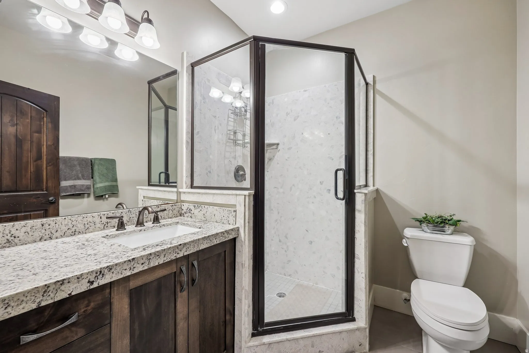 Lower-level full bathroom with a granite dual-sink vanity, bronze fixtures and a glass-enclosed walk-in shower in a Rustler at Hideout home.