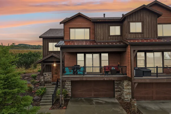 Twilight rendering of the rear elevation with a lit deck and glowing windows in Rustler at Hideout; sky digitally enhanced, deck, siding and view as built.