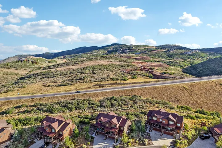 Wide aerial of terraced homes with multi-level decks in Rustler at Hideout, set against open hillside and a mountain backdrop.