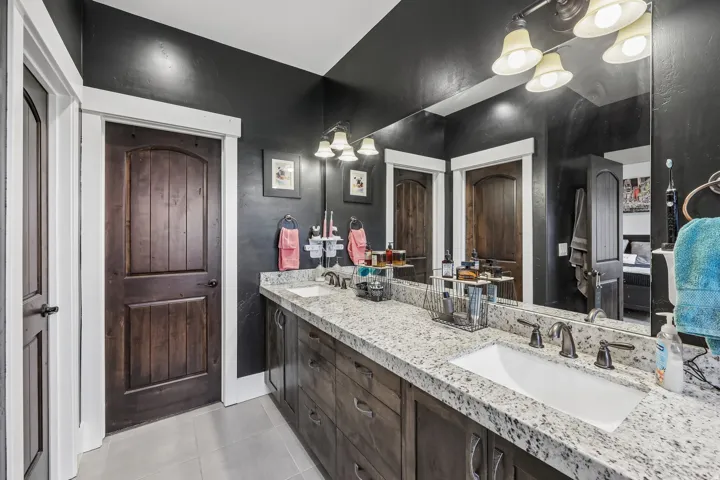 Primary bathroom with a double vanity, speckled stone countertop, dark wood cabinetry and a large mirror in a Rustler at Hideout home.