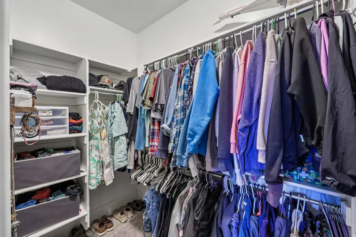 Primary walk-in closet with built-in shelving, multiple hanging rods and carpet flooring in a Rustler at Hideout home.