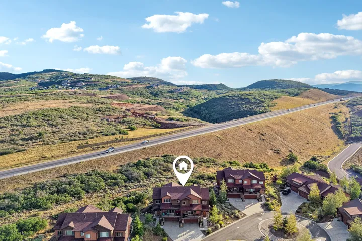 Aerial marking the home's site on a sloped lot in Rustler at Hideout, with multiple balconies, paver driveway and attached garage above Jordanelle Reservoir.