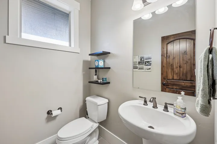 Main-level powder bath off the kitchen with a pedestal sink, bronze faucet and knotty alder door in a Hideout, Utah mountain home.