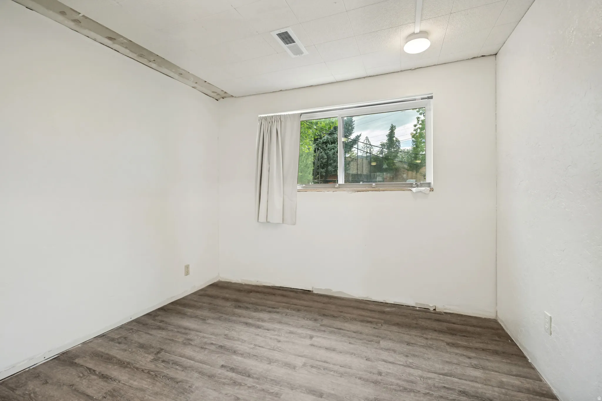Wood-finish flooring with white walls and a single window