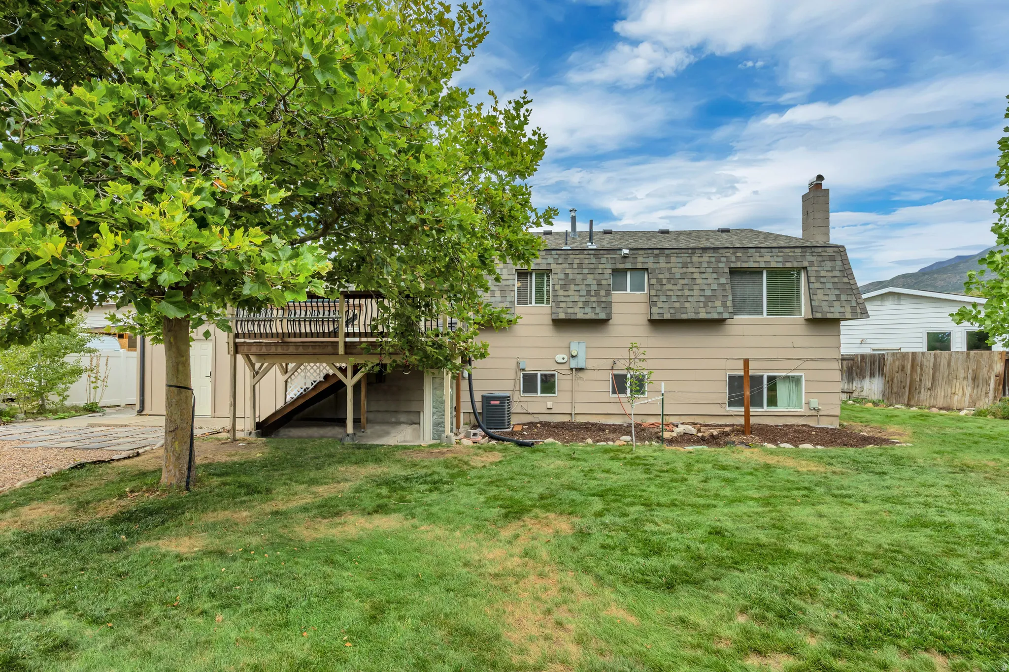 Expansive rear yard featuring a large wooden deck with railing, a sizable lawn, and mature trees