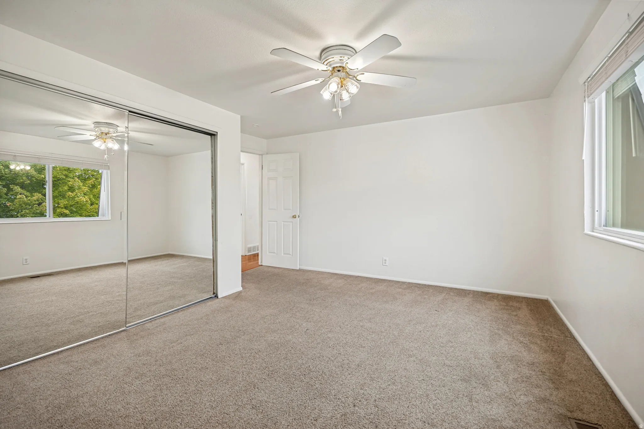 Wall-to-wall carpeting, mirrored sliding closet doors, ceiling fan with integrated lighting, and multiple windows