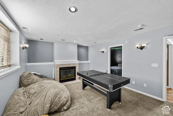 Recessed lighting, wall sconces, stone-surround fireplace with hearth, and carpeted flooring