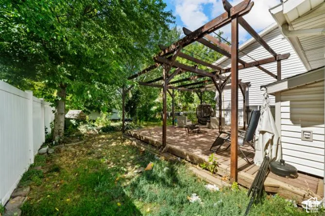 Expansive backyard featuring a white privacy fence, mature trees, a wood deck, and a wood pergola