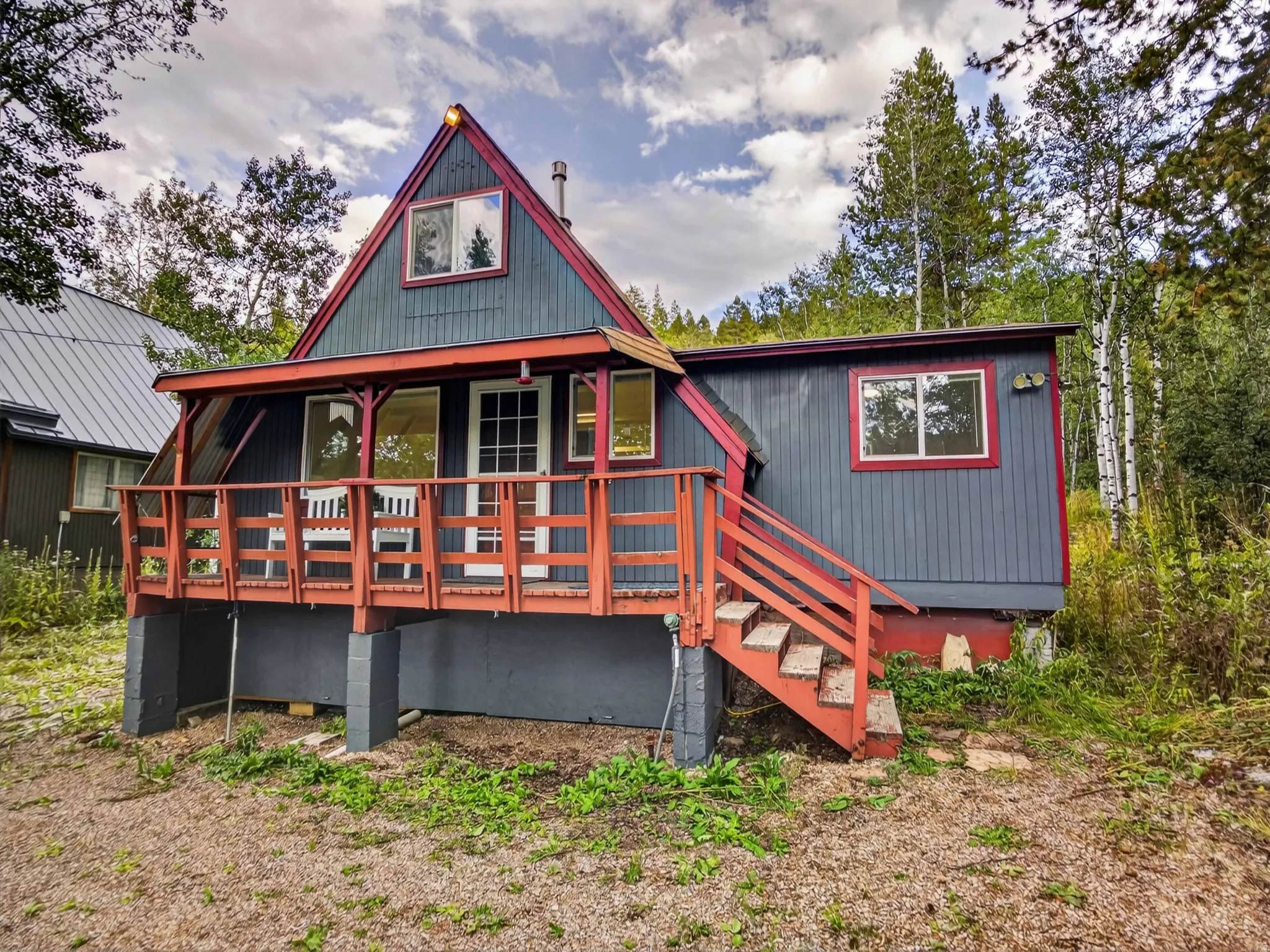 A-frame residence featuring a covered front porch, red trim accents, exterior staircase, and multiple windows
