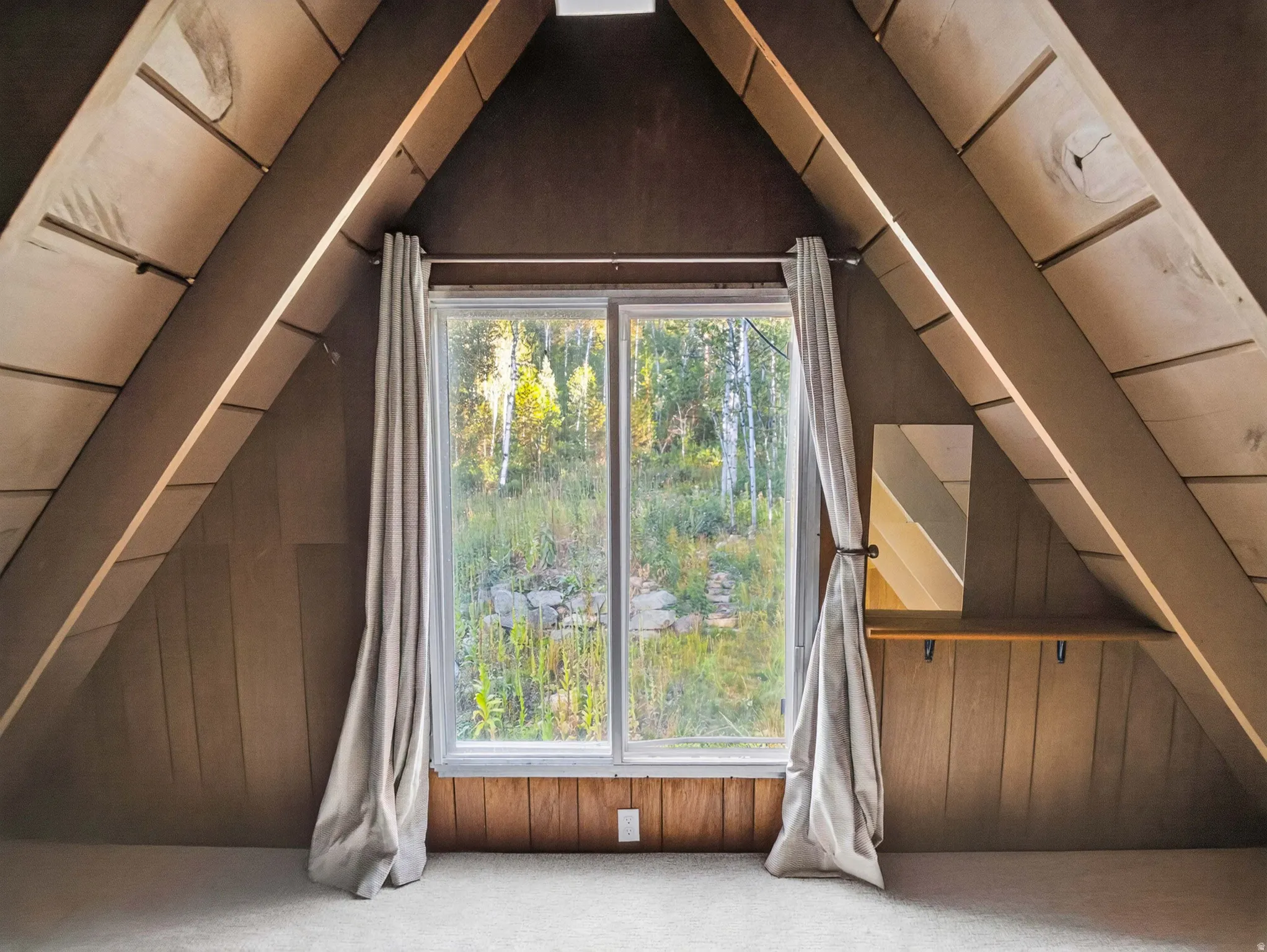 A-frame architectural design with exposed wood beams, wood-paneled walls, a large casement window, and neutral carpeting