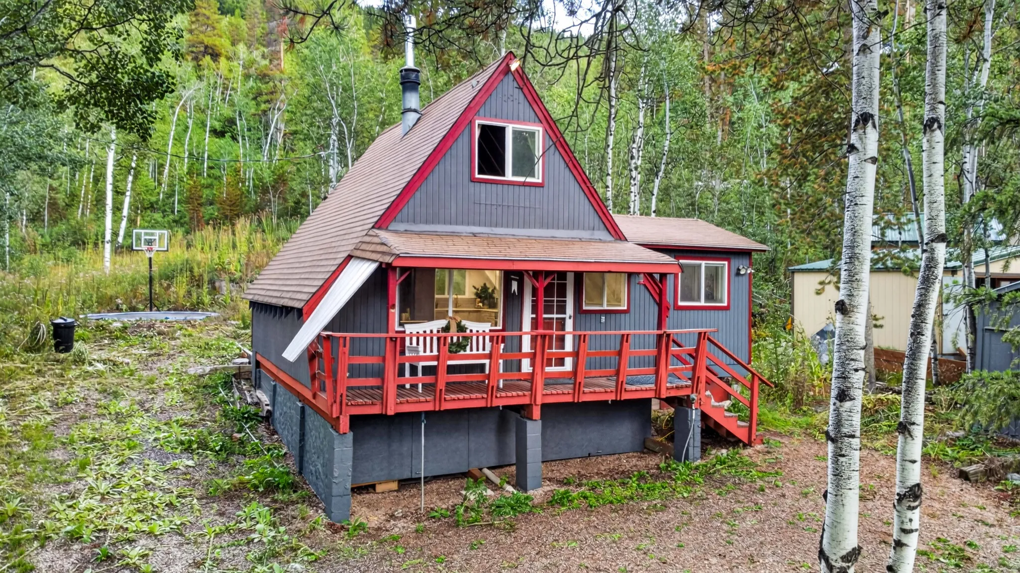 A-frame architecture with a prominent red-trimmed porch, elevated deck, and surrounding mature trees