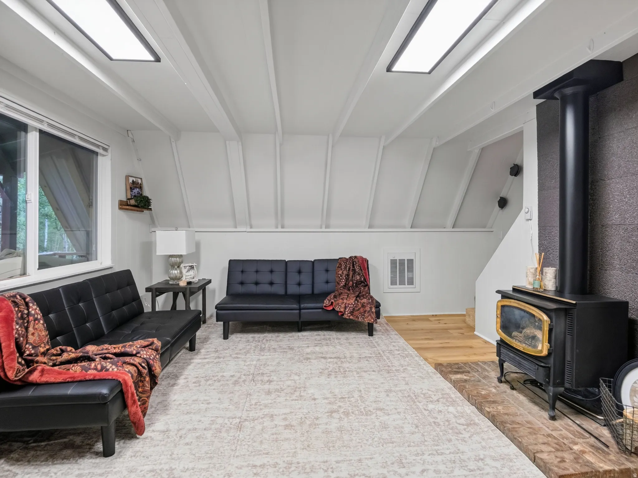 Vaulted ceiling with exposed beams, wood-finish flooring, recessed lighting, and a wood-burning stove with a stone hearth