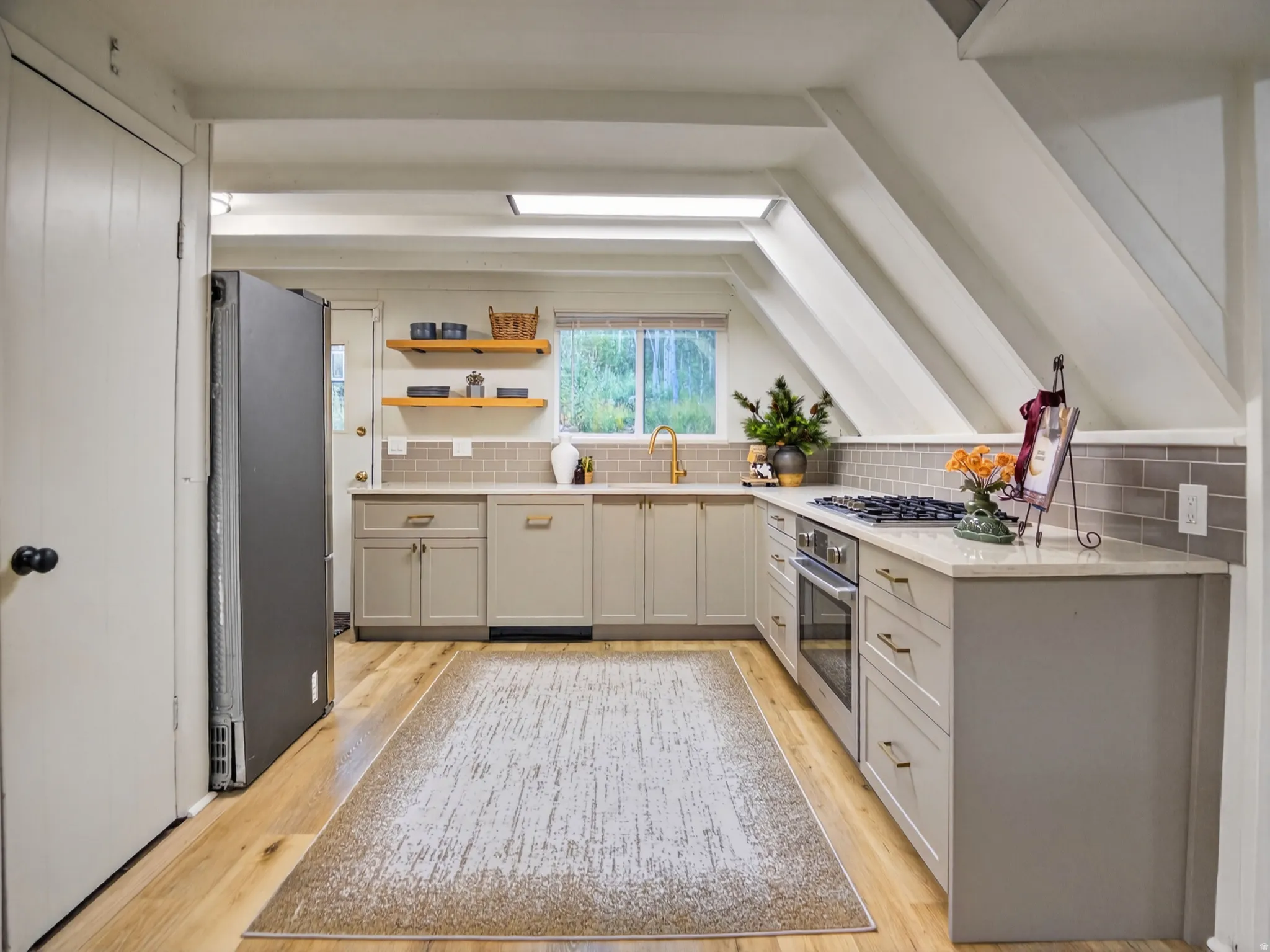 Kitchen featuring wood-finish flooring, light-colored cabinetry with gold-tone hardware, a gas cooktop, built-in oven, and a tile backsplash