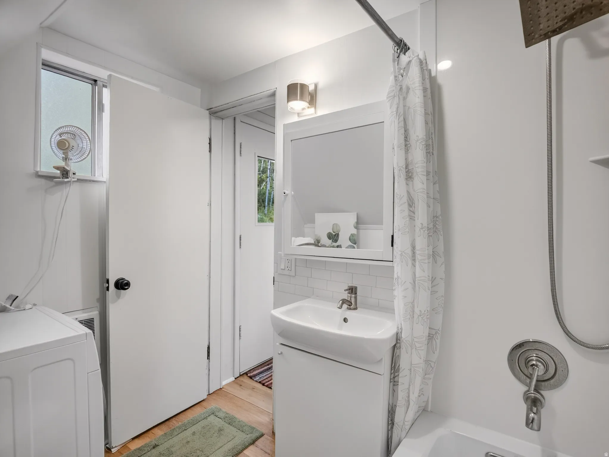 White subway tile backsplash, wall-mounted vanity with integrated sink, brushed nickel faucet, shower/tub combination with brushed nickel fixtures, and light wood-finish flooring