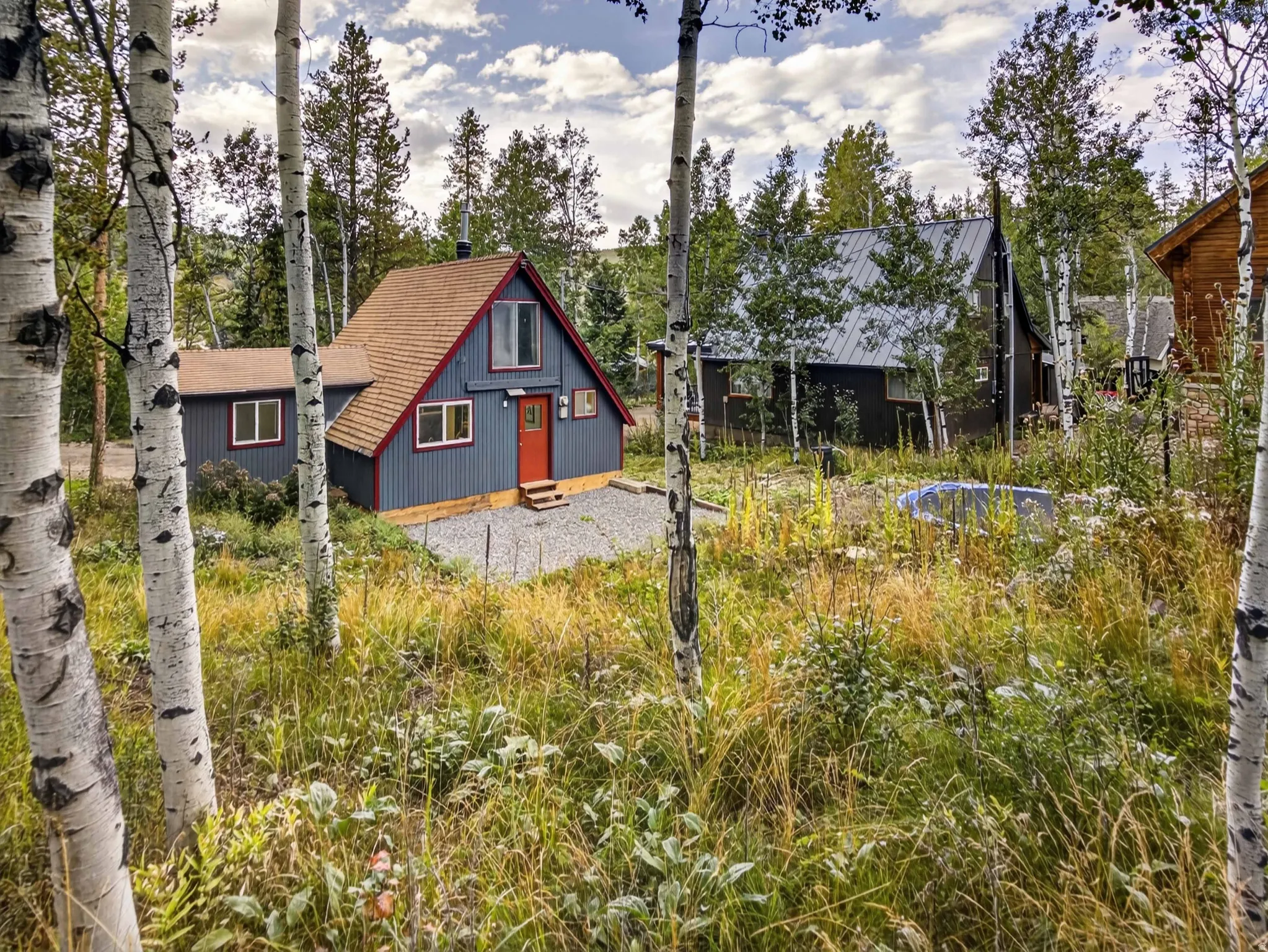 Charming A-frame structure featuring blue siding, red trim, a red entry door, and a brown shingle roof